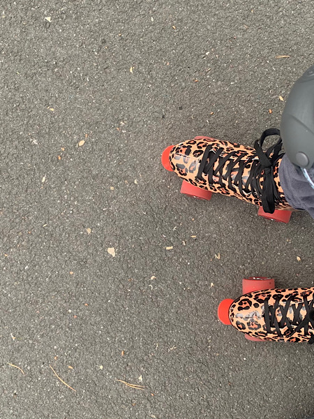 Straßenasphalt und von oben fotografierte Rollerskates im Leopardenmuster mit roten Rollen.