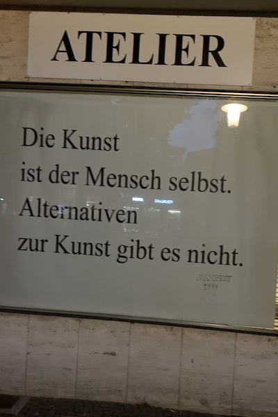 Zwei Schilder, auf dem obersten steht Atelier, auf den unteren Die Kunst ist der Mensch selbst. Alternativen zur Kunst gibt es nicht.