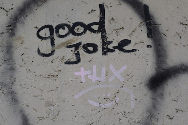 Eine verschmutzte, beschädigte Wand in einem gesprühten Kreis der Tag "good Joke" thx und ein Smiley