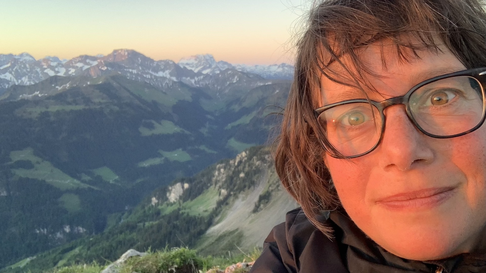 Rechts im Bild Nahaufnahme einer Frau (Gesicht), von der Sonne beschienen im Hintergrund die Vorarlberger Berglandschaft.