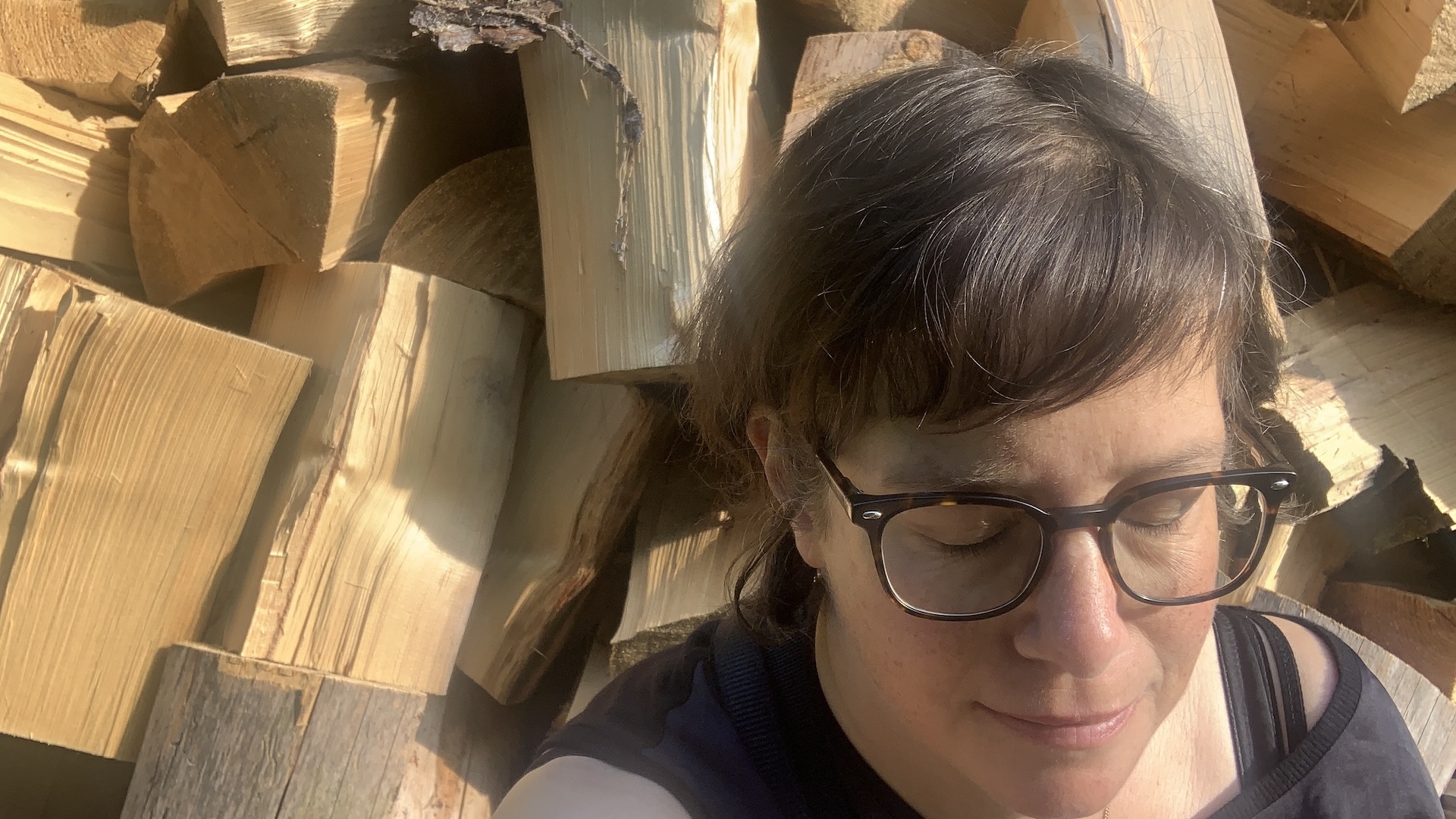 Porträt einer dunkelhaarige Frau, vor einem Holztafel mit geschlossenen Augen sitzend.