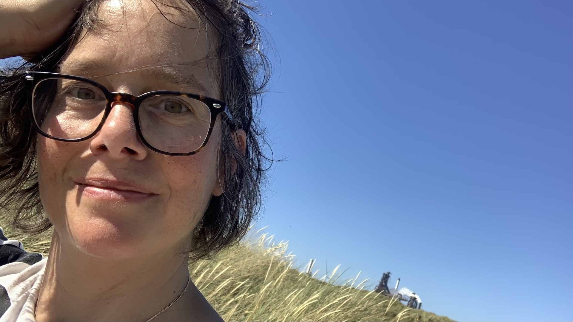 Porträt einer Frau, blauer Himmel und Dünenlandschaft im Hintergrund