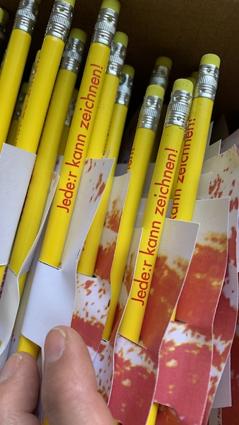 Eine Handvoll gelber Stifte mit der Aufschrift Jede:r kann zeichnen! als Give away für die Gedankenkritzeleien.