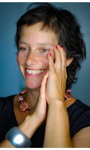 Porträt von Katja Reetz, den Blick leicht nach links gerichtet, fröhlich lächelnd vor graublauem Hintergrund